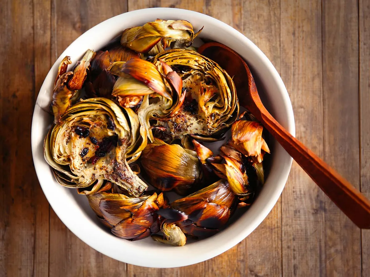 Bol en faïence contenant des fonds d'artichaut braisés, nappés d'une sauce claire aux herbes et citron, posé sur une planche