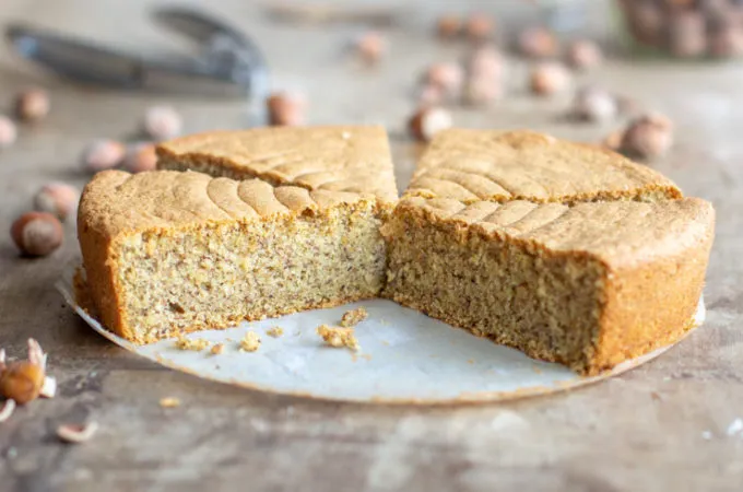Un gâteau rond doré, tranché pour révéler une mie noisette claire, nappé d'un léger voile de praliné brillant et quelques